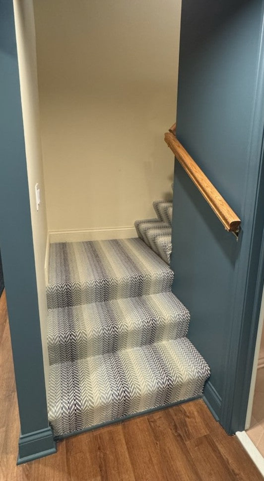 Staircase with striped carpet and wooden handrail in a home setting.